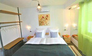 Un dormitorio con cama, dos mesitas de noche, una lámpara colgante, un aire acondicionado de pared y una cortina verde.