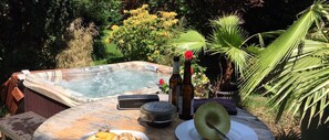 A hot tub surrounded by lush greenery, a wooden table with a bottle, a hat, and a plate with food. - Schacht34 (Oberhausen)