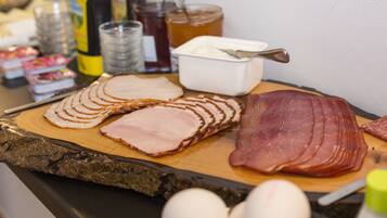A variety of meats and condiments on a wooden board, including sliced ham and bacon, with eggs and jars of honey and jam visible.
