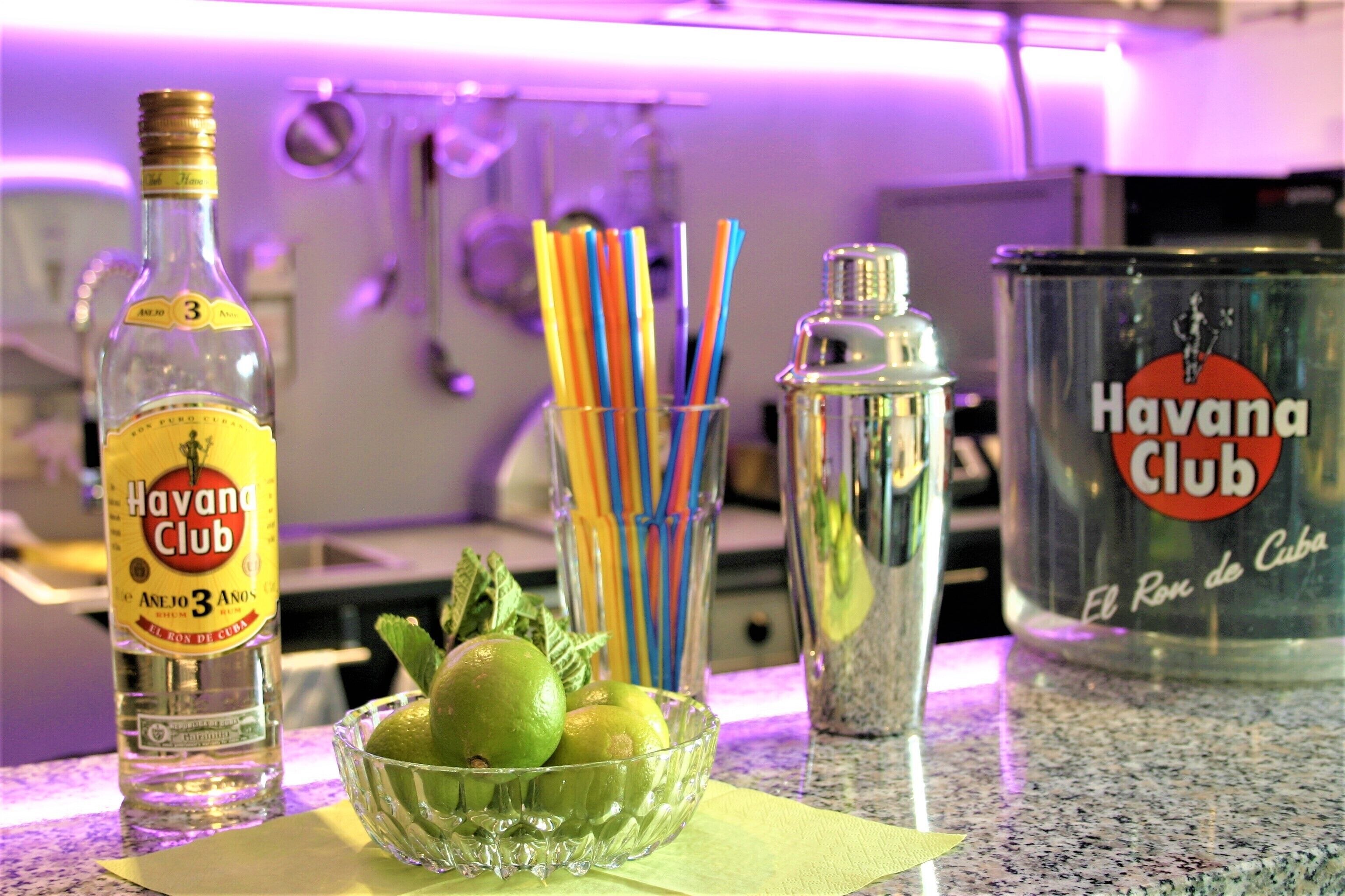 Eine Küchenarbeitsplatte mit einer Havana Club Rumflasche, einem Limettenschnitz, einem Cocktail-Shaker und einer mit Havana Club beschrifteten Dose.