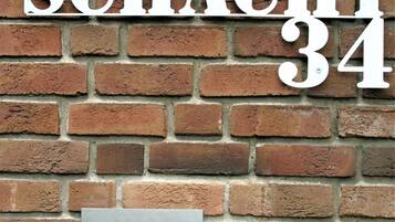 Un mur de briques sur lequel est inscrit le texte « SCHACHT 34 » et où est fixée une boîte aux lettres en métal.
