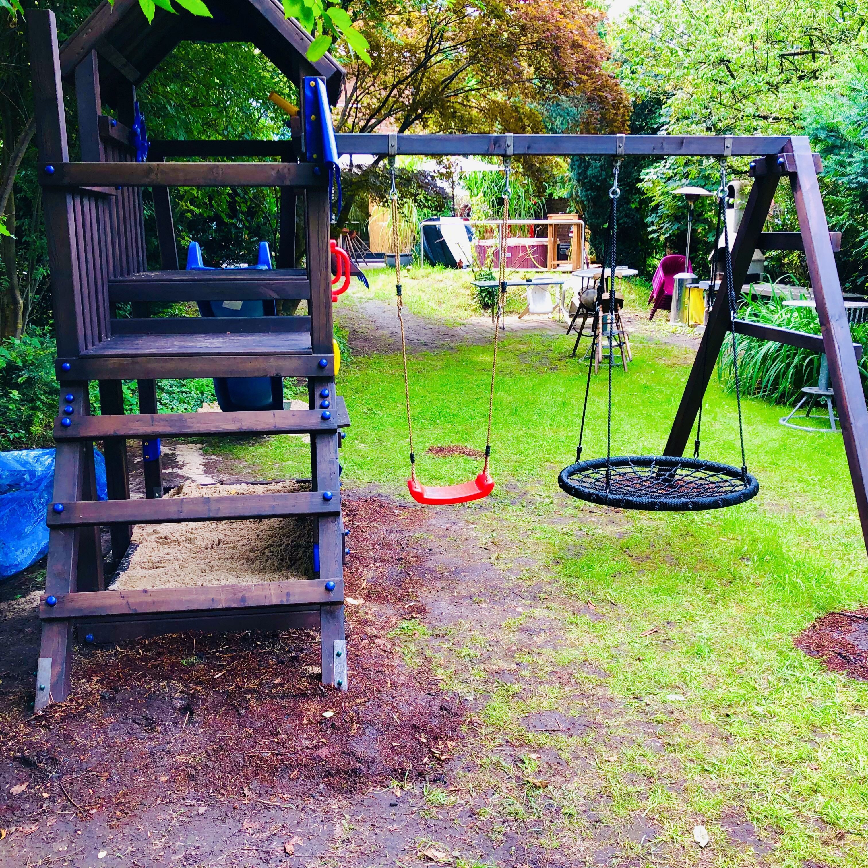 A wooden play structure with a slide and swings in a garden.
