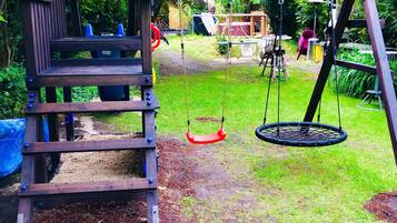 A wooden play structure with a slide and swings in a garden.