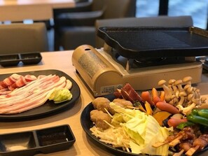 A table with various food items including meat, vegetables, and mushrooms, with a grill and a container of sauces. - Soar Resort (Tsushima)