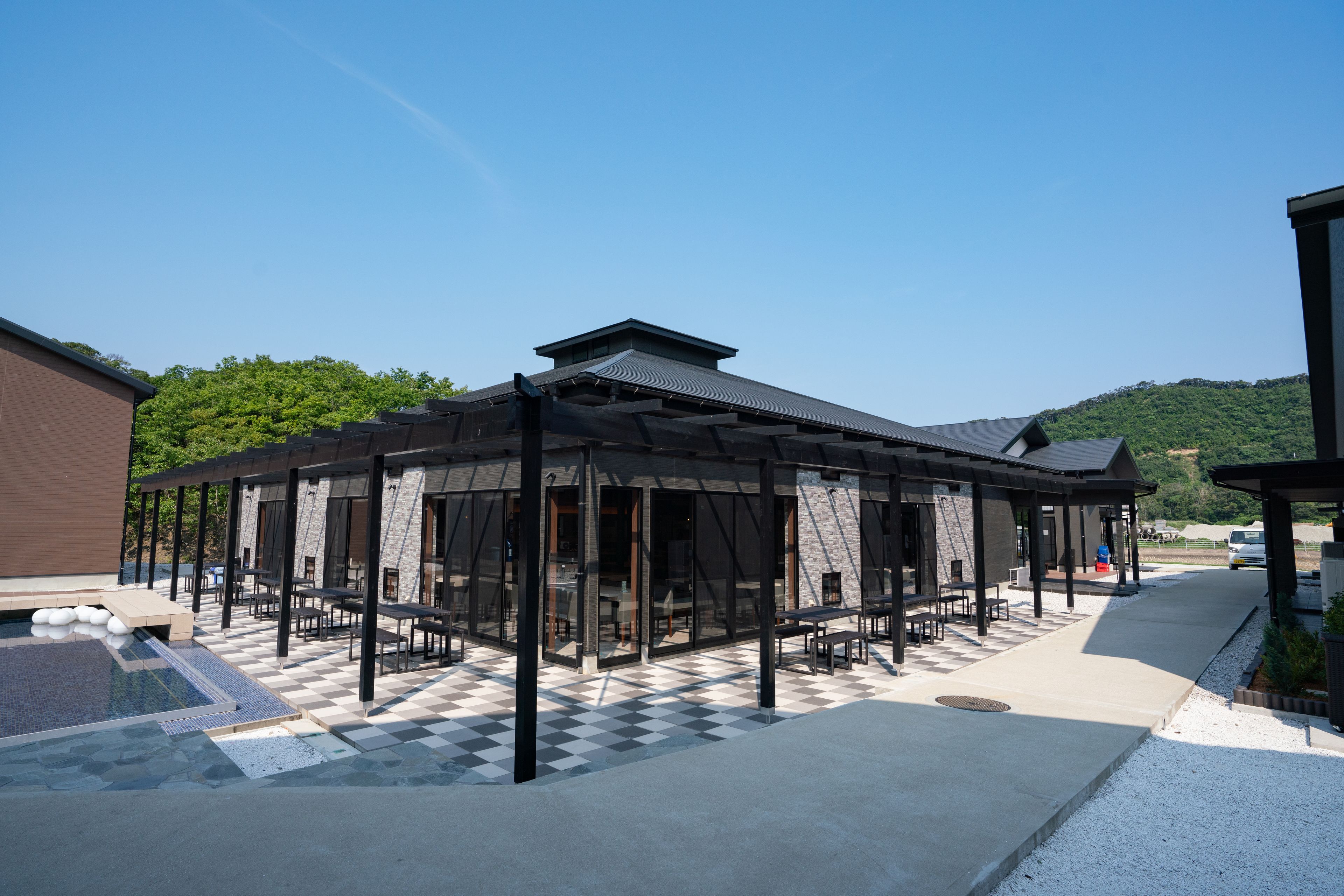A modern outdoor seating area with a checkered floor, glass walls, and a covered section with tables and chairs.