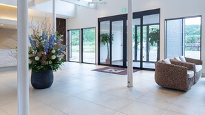 Un hall d’entrée spacieux, doté de hauts plafonds, de grandes fenêtres et d’une plante en pot placée au centre.