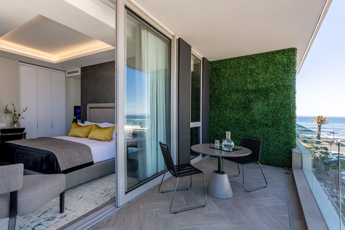 A modern bedroom with a bed, a glass door leading to a balcony, and a view of the ocean.