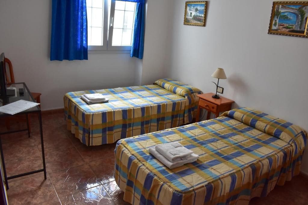 Una habitación con dos camas, un escritorio, una silla, un ventanal con cortinas y decoración en la pared.
