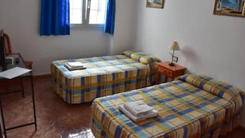 Una habitación con dos camas, un escritorio, una silla, un ventanal con cortinas y decoración en la pared.
