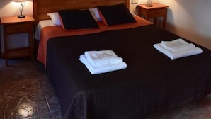 A hotel room with a bed, two bedside tables, a nightstand, a painting on the wall, and a ceiling light fixture.