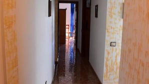 A hallway with a tiled floor and walls with a yellowish pattern. There are doors on the right and a visible door at the end of the hallway.