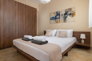 A neatly made bed with towels, a wooden wardrobe, and abstract art on the wall.