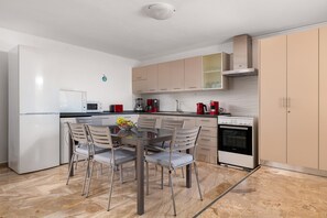A modern kitchen with white cabinets, a dining table with chairs, a microwave, a coffee maker, and an oven.