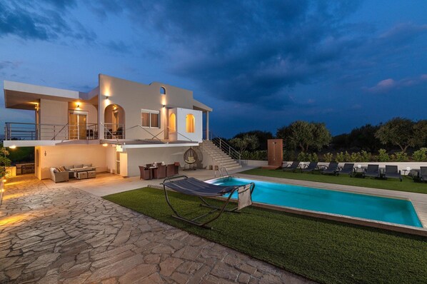 A modern two-story house with a swimming pool, outdoor seating, and a staircase leading to a balcony.