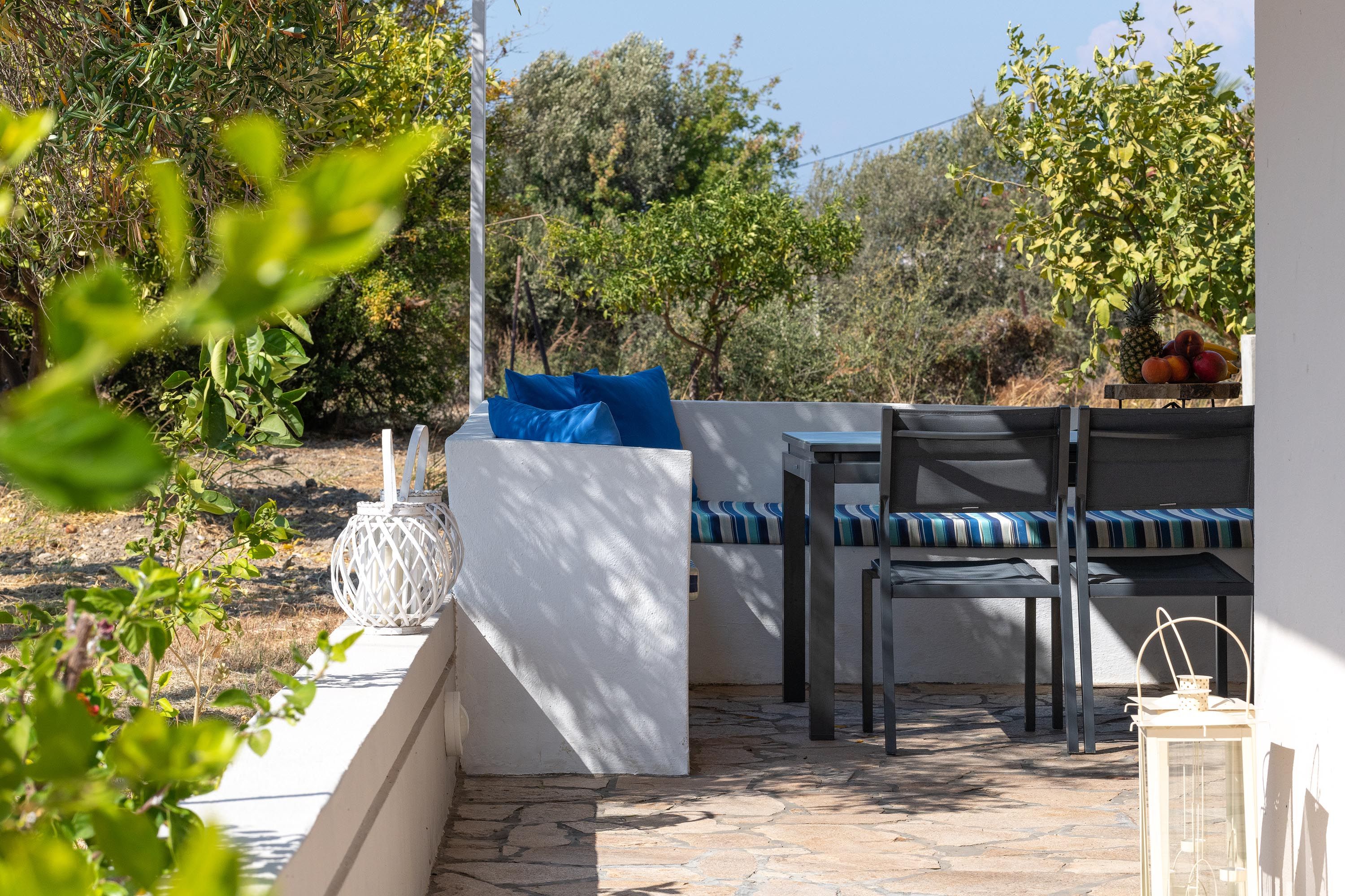 An outdoor seating area with a table and chairs, a white wall, and a stone floor.