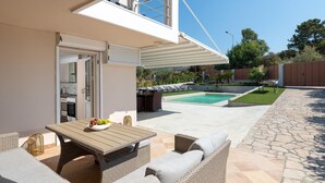 En moderne udendørs terrasse med pool, fletmøbler og udsigt til baghaven.