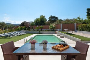 Un'area piscina con tavolo in vetro, sedie in vimini e un vassoio di pasticcini.