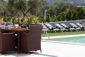 Area piscina con mobili in vimini, un tavolo con pasticcini e bevande, e poltrone relax.