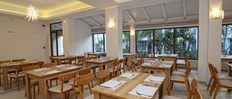 A spacious dining area with wooden tables and chairs, large windows, and modern lighting fixtures.