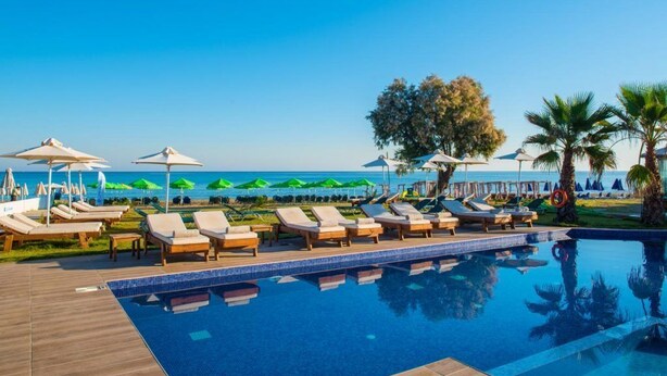 Un espace aménagé au bord de la piscine, avec des chaises longues et des parasols, un ciel d’un bleu éclatant et une vue sur l’océan.