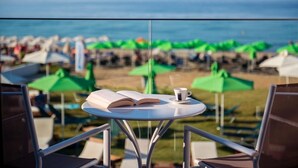 Une table avec un livre ouvert et une tasse, donnant sur une plage parsemée de parasols.