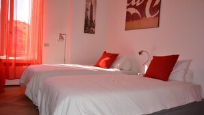 Una habitación de hotel con dos camas, ropa de cama roja y blanca, un cartel con un paisaje urbano y un letrero de Coca-Cola.
