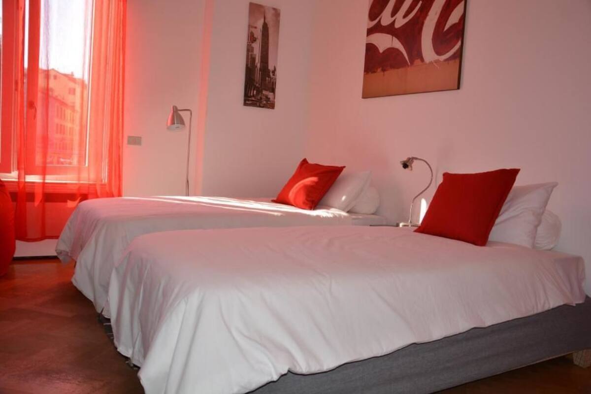 Una habitación de hotel con dos camas, ropa de cama roja y blanca, un cartel con un paisaje urbano y un letrero de Coca-Cola.