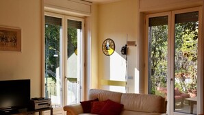Un salón con un sofá color crema, un televisor de pantalla plana y un ventanal con vistas a zonas verdes.