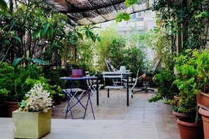 An outdoor patio area with a table and chairs, surrounded by potted plants and a thatched roof structure. - Casa della Vetra (Milan)