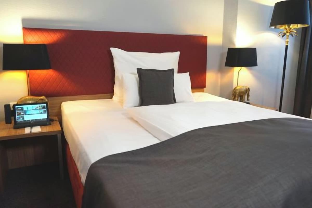 A hotel room with a bed, two bedside lamps, a nightstand with a laptop, and a decorative elephant figure.