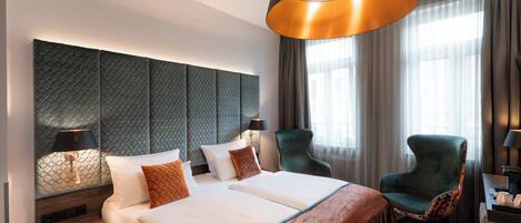 Una habitación de hotel moderna con una cama grande, dos sillones, un escritorio y un ventanal con cortinas.