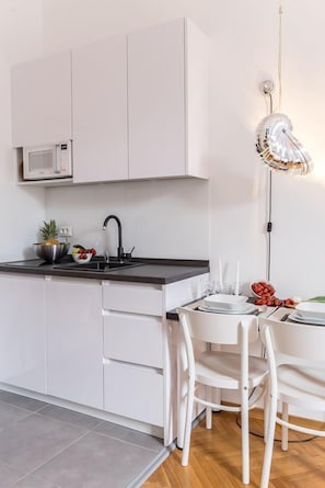 Eine moderne Küche mit weißen Schränken, einer schwarzen Arbeitsplatte, einer Mikrowelle, einem Spülbecken und einem Essbereich mit weißen Stühlen und einem Tisch für zwei Personen.