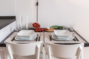A dining table set with white plates, cutlery, and glasses, with a bowl of strawberries and a bulb of garlic on the table. - F11 Gallery (Zagreb)