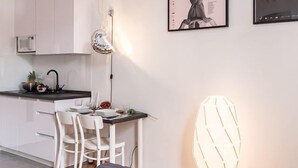 Una cocina moderna con armarios blancos, un comedor con una mesa y sillas blancas, y una lámpara colgante.
