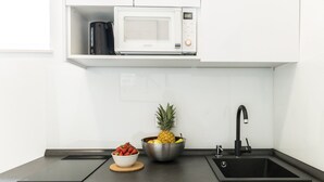 Una cocina con microondas, un lavamanos, un tazón de fresas y un tazón de fruta.