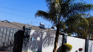 A residential area with a white house, a black gate, a palm tree, and a small bush. - Flamboyant Place (Harare)