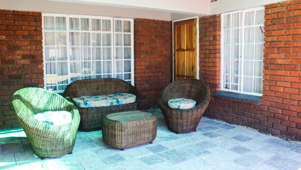 A covered patio area with wicker furniture, including two chairs and a small ottoman, and a brick wall. - Flamboyant Place (Harare)