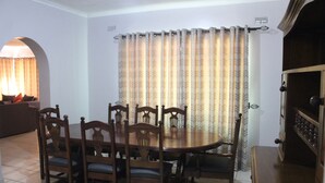 A dining room with a wooden table and chairs, a sofa, and a window with patterned curtains. - Flamboyant Place (Harare)