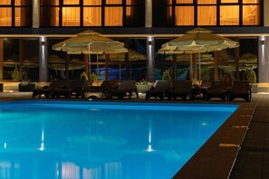 A swimming pool with lounge chairs and umbrellas, surrounded by a building with large windows. - Toga (Yablunytsia)