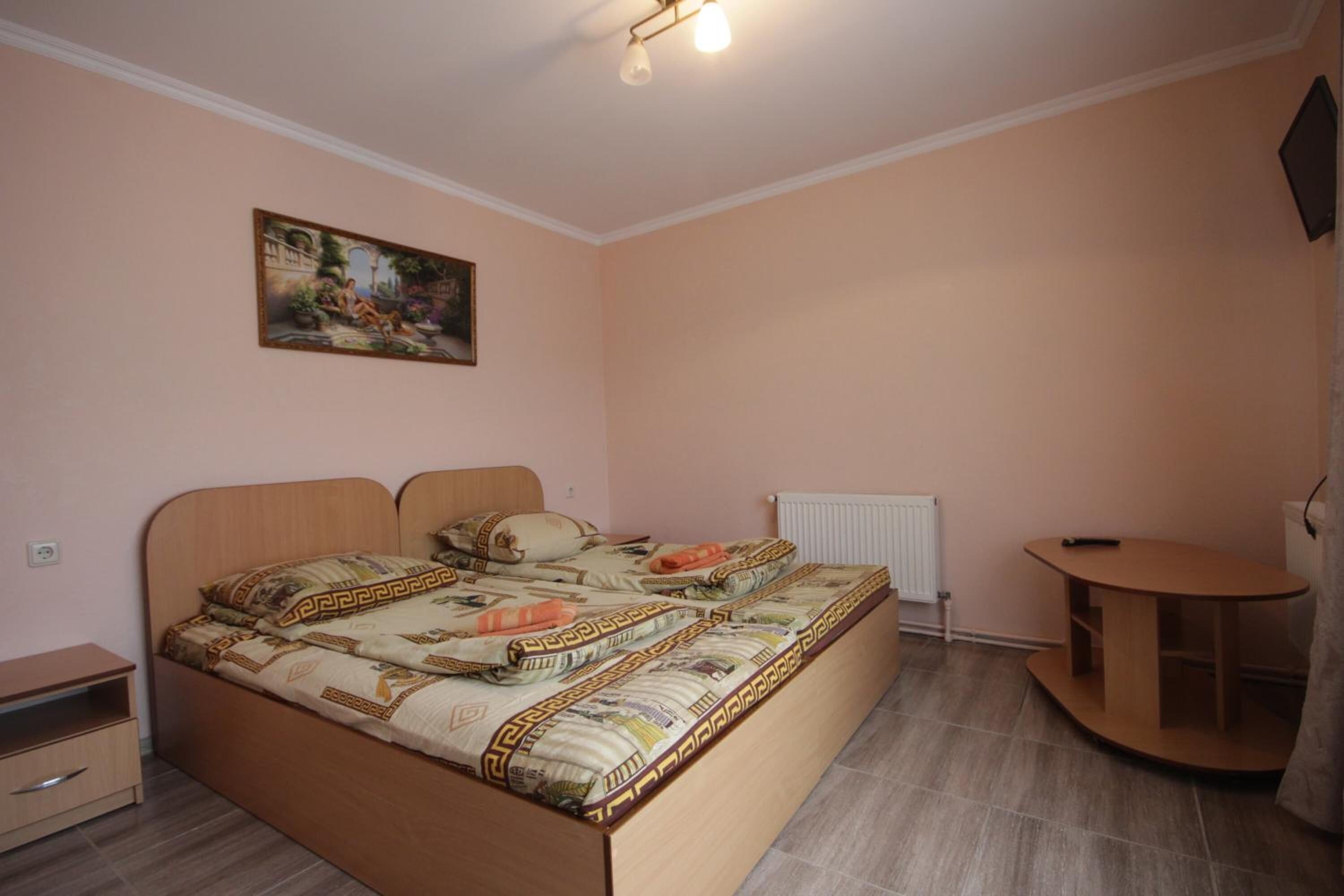 Un dormitorio con una cama, una mesita de noche, una pequeña mesa de madera, un radiador y un cuadro en la pared.
