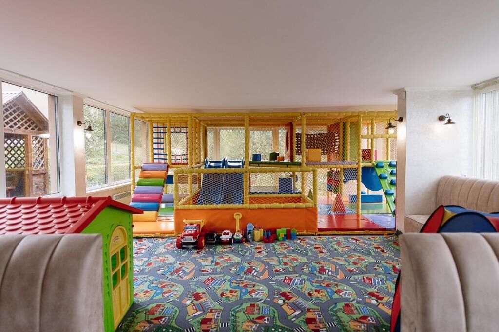 A playroom with a colorful playhouse, a soft play area, and a patterned carpet.