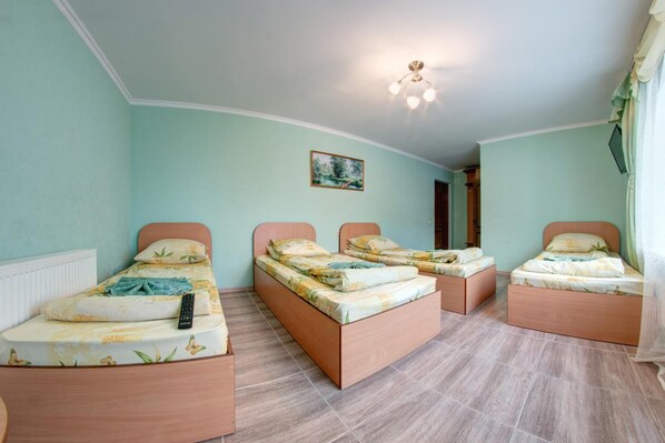 Una habitación con tres camas individuales, cada una con estructura de madera y ropa de cama floral. Hay una lámpara en el techo y un cuadro en la pared.