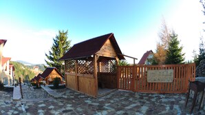 Ein rustikales Holzen Gebäude mit rotem Dach, möglicherweise ein Gasthaus oder eine kleine Lodge, umgeben von gepflastertem Steinweg und Holzzaun.