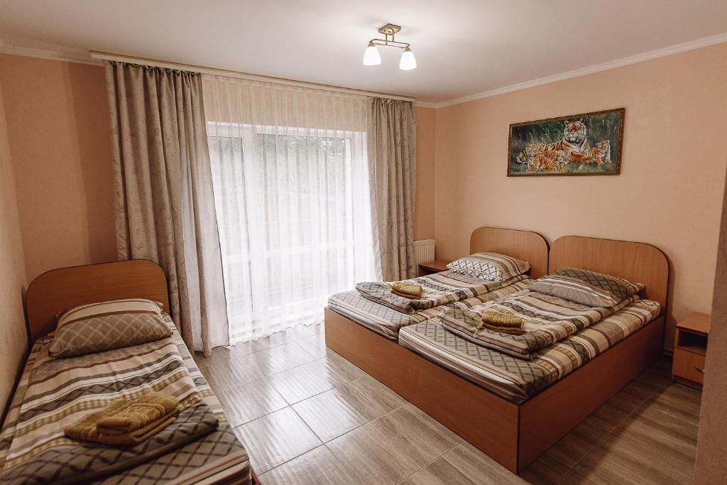 A bedroom with two beds, a window with curtains, a painting on the wall, and a bedside table.