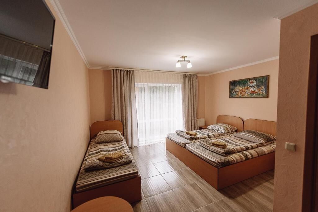 Una habitación con dos camas, una ventana con cortinas, un cuadro en la pared y una lámpara en el techo.