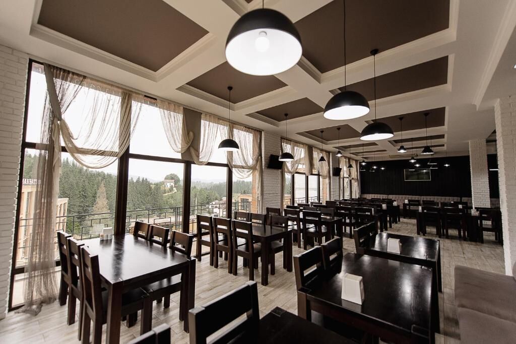 A spacious dining area with multiple tables and chairs, large windows with curtains, and pendant lighting.