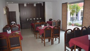 A dining area with multiple tables and chairs, a wooden partition wall, and a view of the outside through large glass doors.