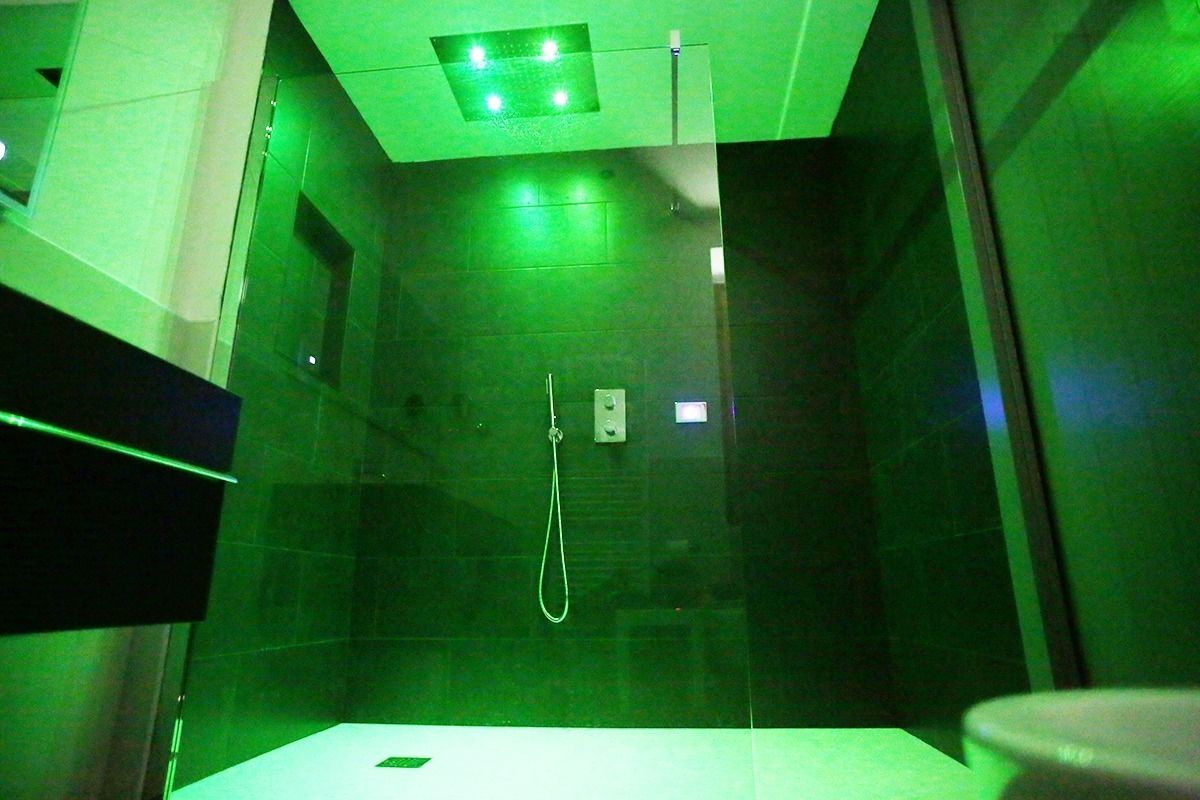 A modern bathroom with a glass-enclosed shower, a visible control panel, and a green-lit ceiling.