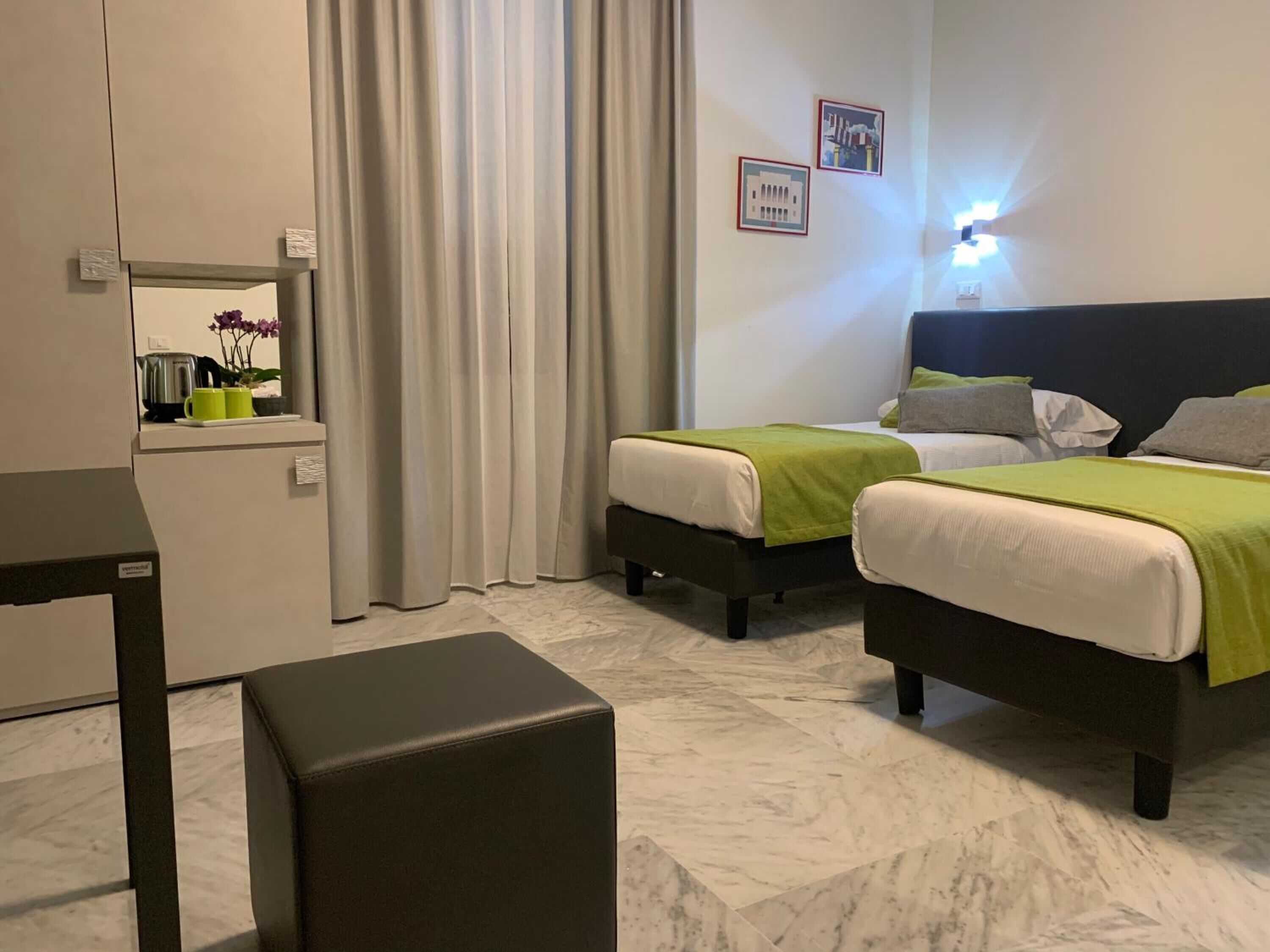 Habitación de hotel con dos camas, una mesita, un banco y un espejo.
