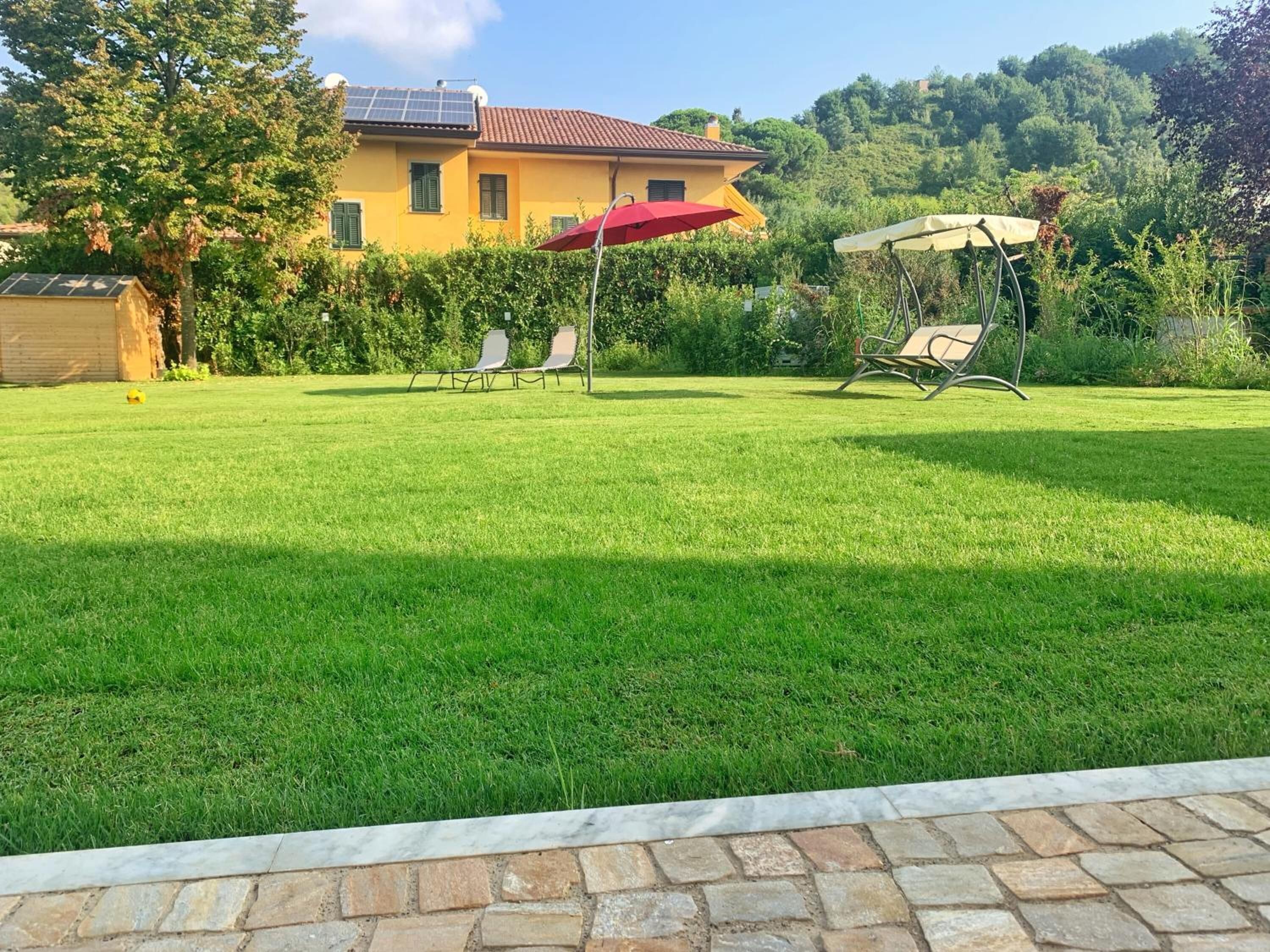 A well-maintained lawn with a patio area, a yellow building with a red roof, and a hill in the background.